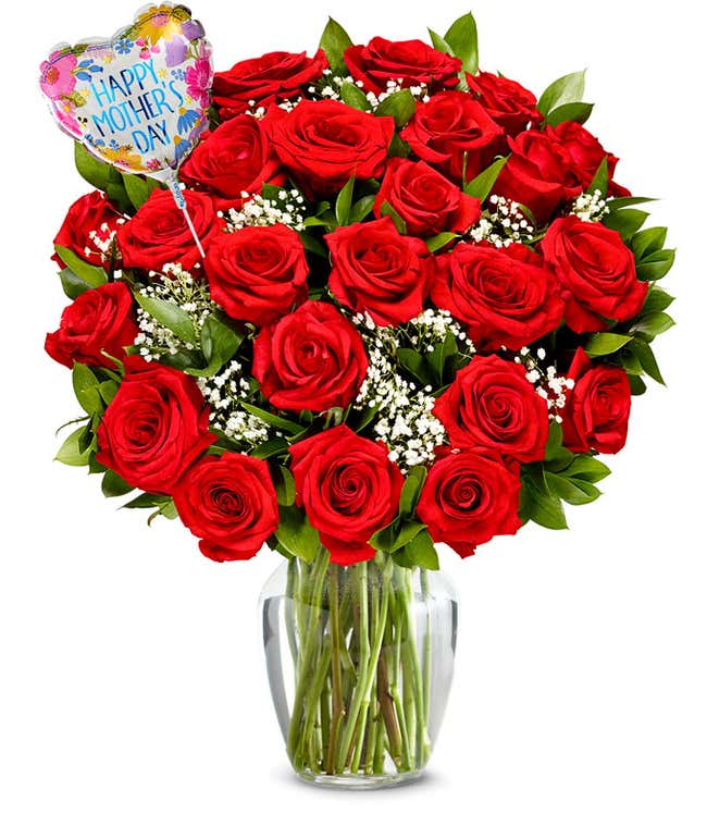 Two dozen red roses with pops of greenery and white baby's breath in a clear glass vase with a pink and red heart shaped balloon reading happy mother's day. 
