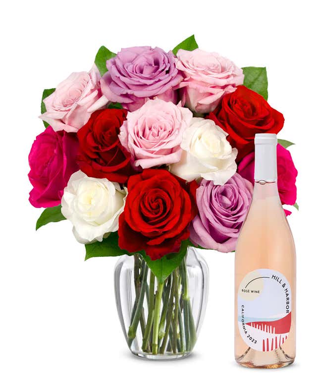 One dozen pink, purple and red roses arranged in a clear glass vase sits beside a bottle of Hill &amp; Harbor California Ros&eacute;.