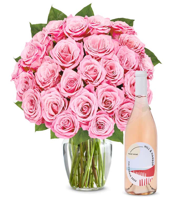 A bouquet of 24 soft pink roses arranged in a clear glass vase is displayed next to a bottle of Hill &amp; Harbor California Ros&eacute;.