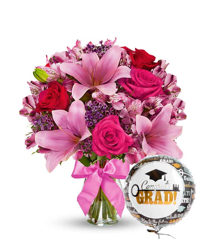 A bursting full bouquet of red and pink flowers including roses, lilies, and more. Next to a congratulations mylar balloon. 
