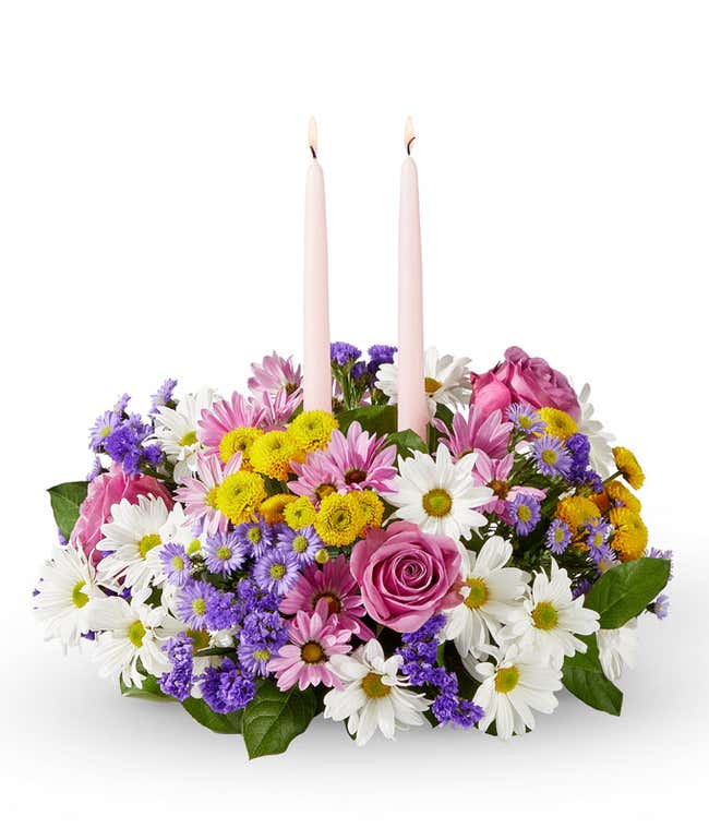 Easter Centerpiece with Lavender Roses, Lavender Daisy Poms, Blue Statice, White Daisy Poms, Yellow Button Poms. and Floral Greenery with Light Pink Taper Candled