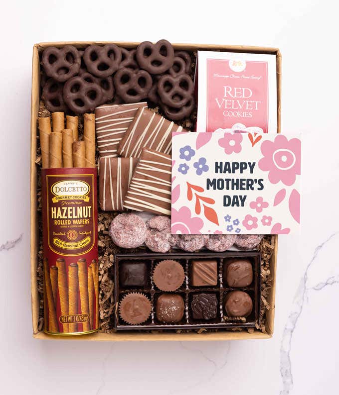 A gift filled with chocolate-covered pretzels, mini chocolate chip cookies, and a box of assorted chocolates. A card reading 'Happy Mother's Day' rests beside the treats.
