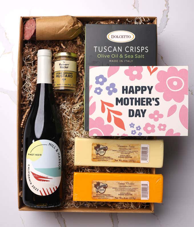 A snack and wine gift box featuring 2 cheeses - chaddar & Swiss, cracker crisps, summer sausage, mustard, and a bottle of red wine. A 'Happy Mother's Day,' sits on top. A perfect gift for Mom.
