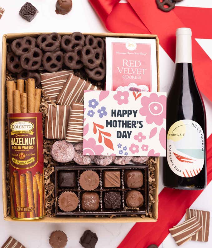 A bottle of Hill & Harbor Pinot Noir, a box of assorted chocolates, chocolate-covered pretzels, and mini chocolate chip cookies with a 'Happy Mother's Day' card placed above.