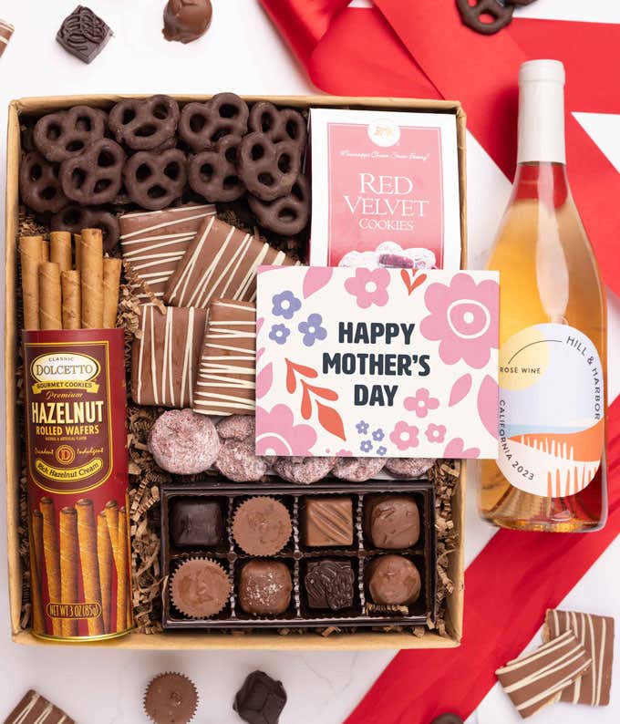 A bottle of Hill & Harbor rosé wine, a box of assorted chocolates, chocolate-covered pretzels, and mini chocolate chip cookies with a 'Happy Mother's Day' card placed above.
