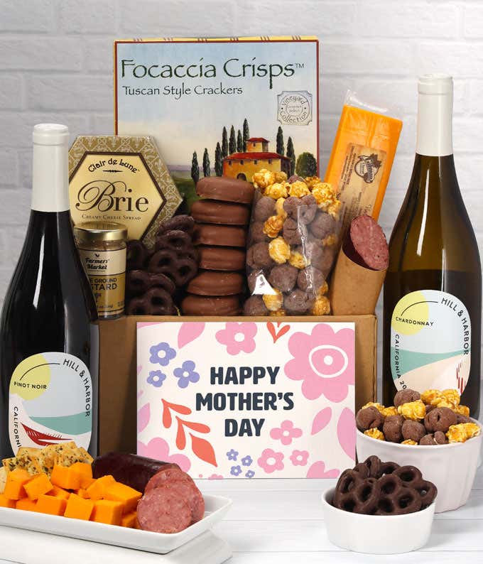 A spread featuring two bottles of wine, 2 cheeses, summer sausage, crackers, chocolate pretzels, caramel corn, and chocolate covered Oreos with a 'Happy Mother's Day' card.