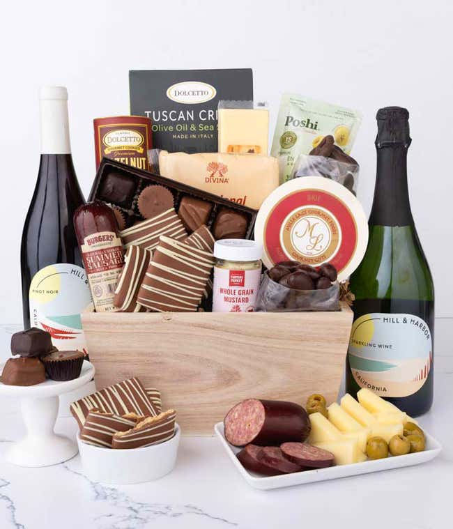 Wooden crate filled with gourmet snacks and two bottles of Hill &amp; Harbor wine,  Sparkling Wine and Pinot Noir, alongside artisan summer sausage, creamy cheeses, assorted chocolates, striped chocolate-covered grahams, cookies, crisps, mustard, and olives.