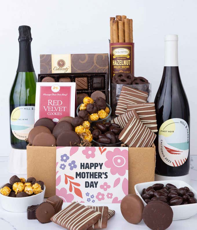 Two bottles of wine - red & sparkling, sit beside chocolate-covered pretzels, mini chocolate chip cookies, caramel popcorn, assorted chocolates, mini buckeyes, chocolate covered Oreos, and a Happy Mother's Day card.