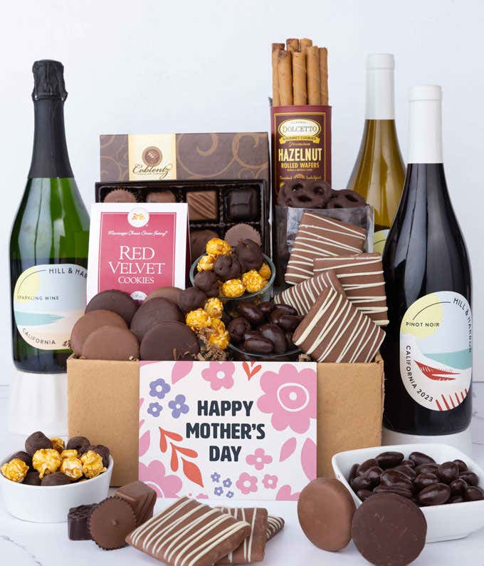 Three bottles of wine - red, white & sparkling, sit beside chocolate-covered pretzels, mini chocolate chip cookies, caramel popcorn, assorted chocolates, mini buckeyes, chocolate covered Oreos, and a Happy Mother's Day card.