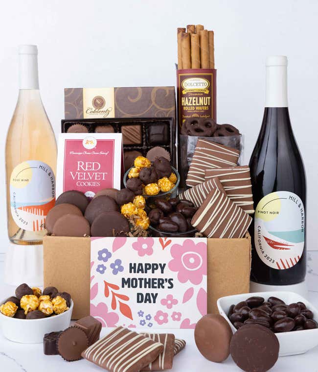 Two bottles of wine - red &amp; ros&eacute;, sit beside chocolate-covered pretzels, mini chocolate chip cookies, caramel popcorn, assorted chocolates, mini buckeyes, chocolate covered Oreos, and a Happy Mother's Day card.