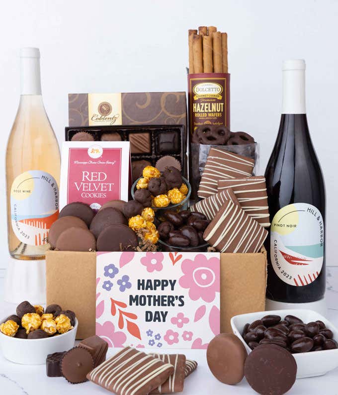 Two bottles of wine - red & rosé, sit beside chocolate-covered pretzels, mini chocolate chip cookies, caramel popcorn, assorted chocolates, mini buckeyes, chocolate covered Oreos, and a Happy Mother's Day card.