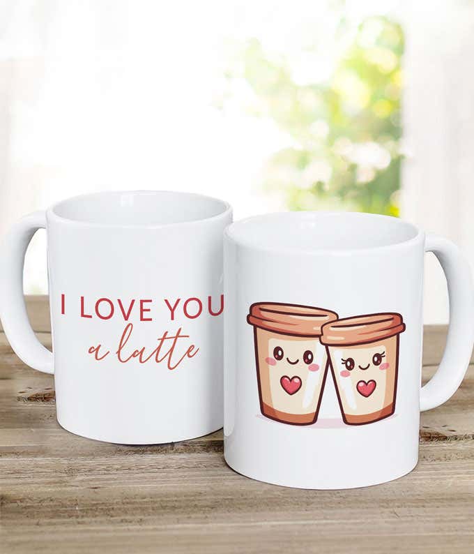 wo white coffee mugs, one reading ‘I love you a latte’ and the other featuring an illustration of two smiling coffee cups with heart details, displayed on a rustic wooden surface.